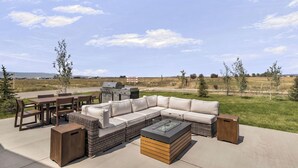 An outdoor patio with a sectional sofa, dining table, chairs, and a grill.