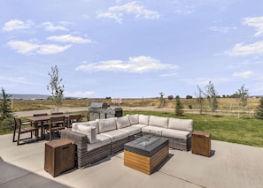An outdoor patio with a sectional sofa, dining table, chairs, and a grill.