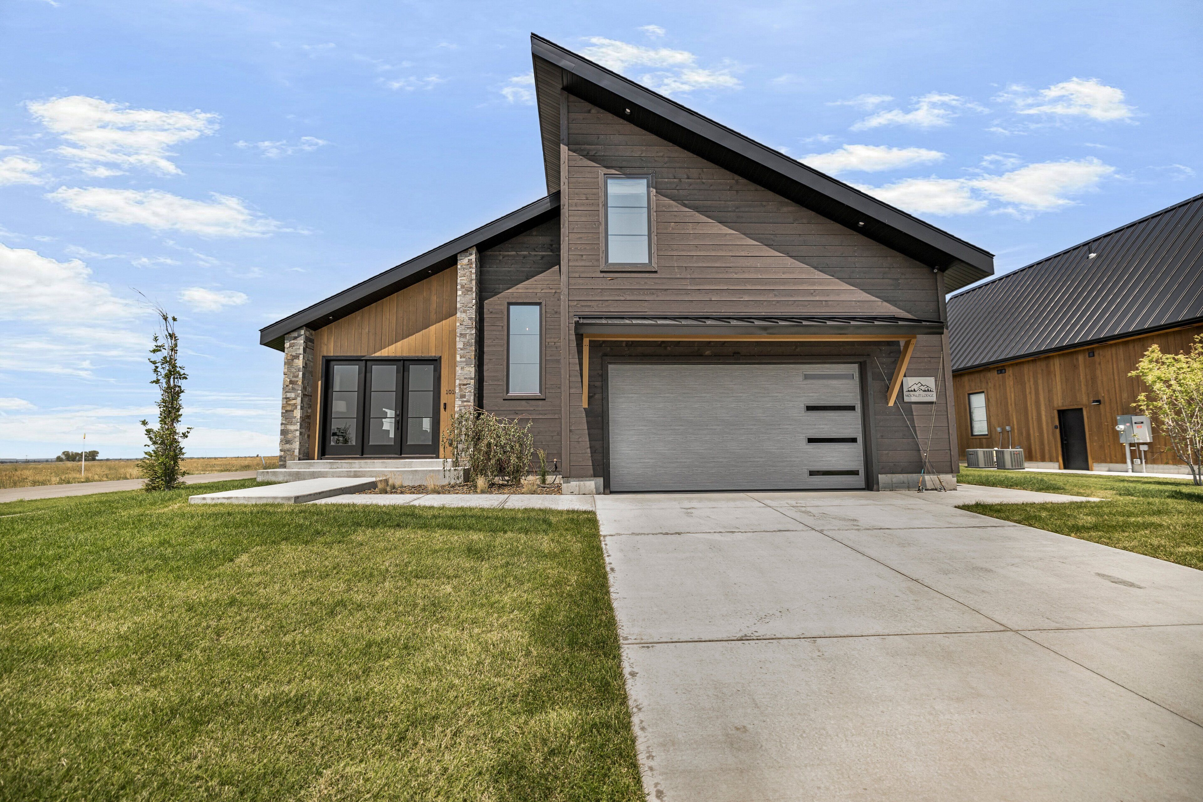 A modern two-story house with a garage, a stone accent wall, and a well-maintained lawn.