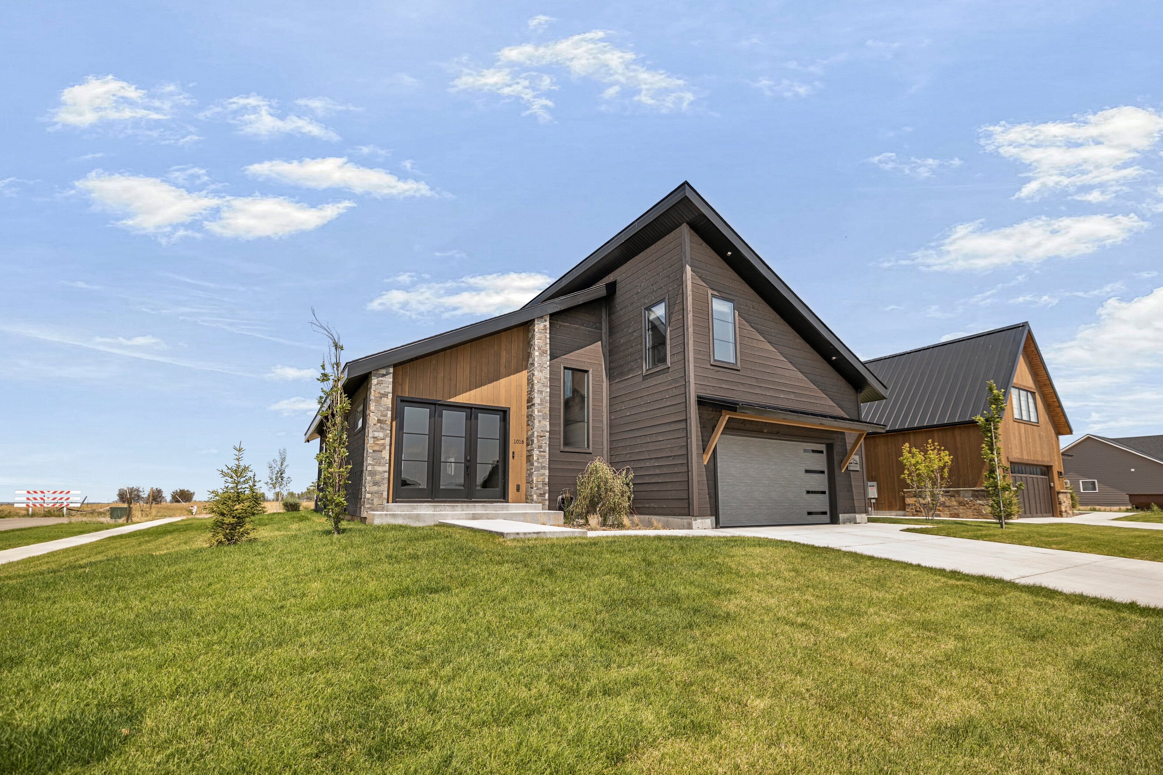 A modern two-story house with a large garage, a well-maintained lawn, and a clear sky.