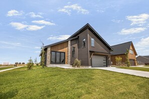 A modern two-story house with a large garage, a well-maintained lawn, and a clear sky.
