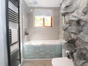 A bathroom with a bathtub, a shower, a sink, and a toilet. There is a window with a view of greenery outside. - The Cottage O'ergate (Hope Valley)