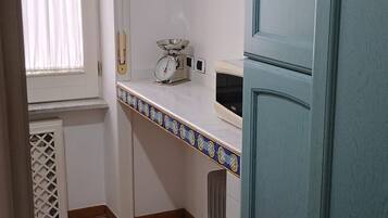 A kitchen with a tiled floor, a window with curtains, a weighing scale, and a blue cabinet.