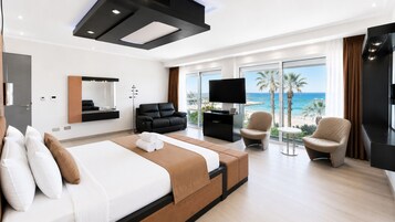 Habitación de hotel moderna con una cama grande, una zona de estar con vista a la playa y un televisor de pantalla plana.