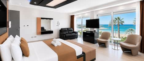 A modern hotel room with a large bed, a sofa, a desk, and a TV. There is a balcony with a view of the ocean.