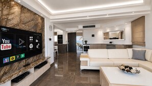 Ein modernes Wohnzimmer mit Flachbildfernseher an einer Marmorwand, einem weißen Sofa und einem Couchtisch mit Dekoration.