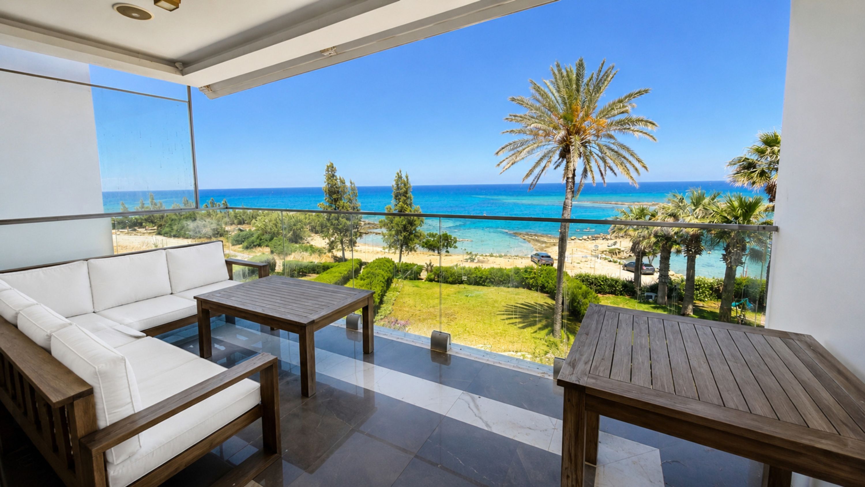 Ein Balkon mit einer weißen Couch, einem Holztisch und Blick auf Strand und Meer.