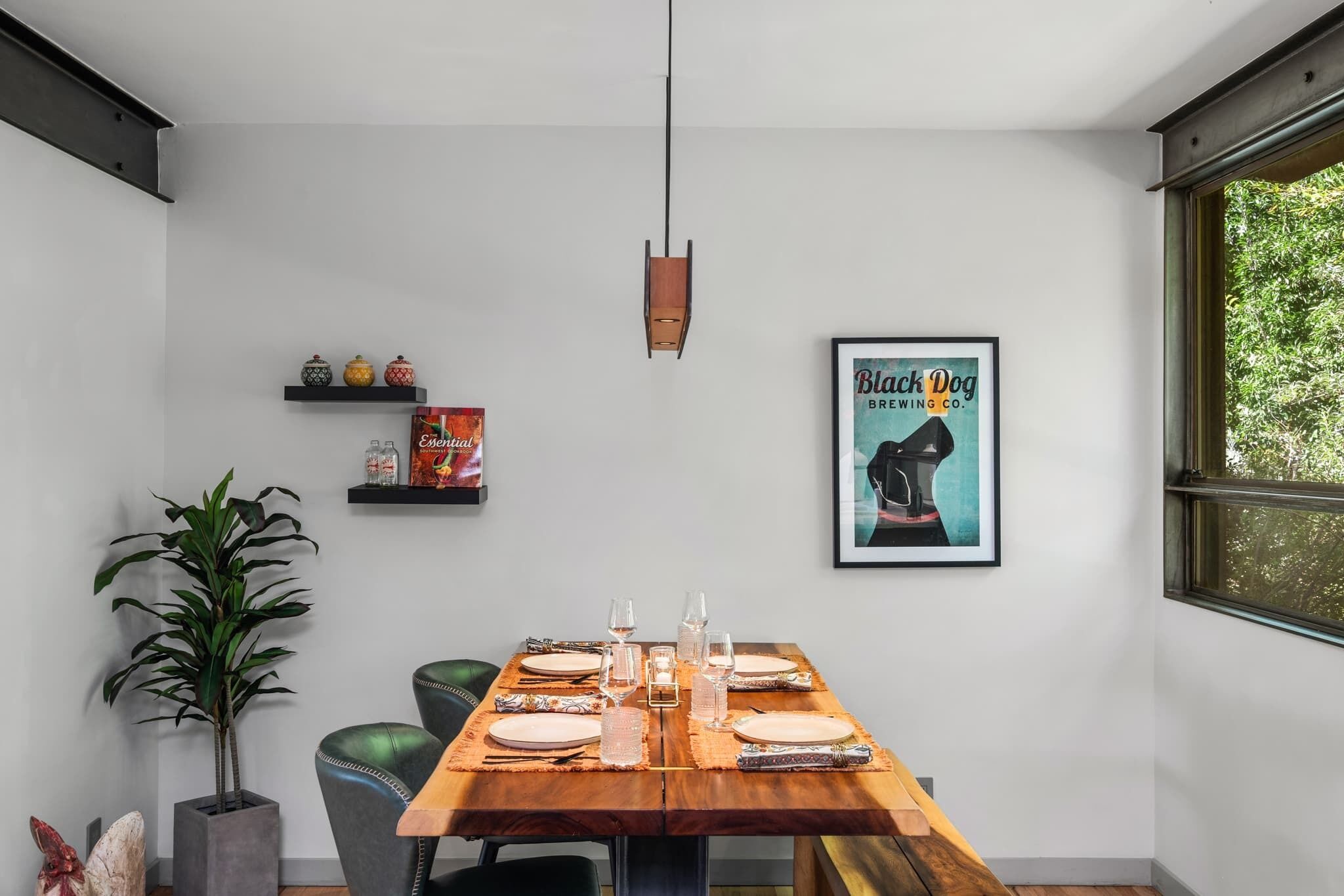 A dining area with a wooden table set for four, a potted plant, and a framed poster on the wall.