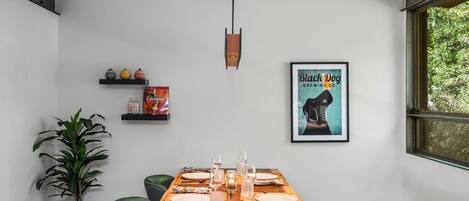 Un coin repas avec une table en bois dressée pour quatre personnes, une plante en pot et une affiche encadrée accrochée au mur.