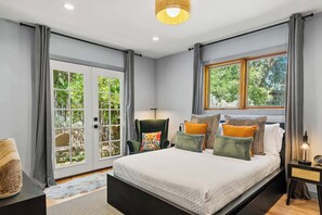 Ein Schlafzimmer mit einem Bett, einem Sessel, einer Lampe und einem Fenster mit Blick auf Bäume.