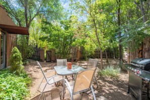 Una veranda esterna con tavolo e sedie, circondata da alberi e un barbecue.
