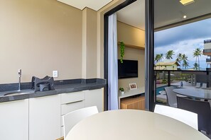 A modern kitchen with a black countertop, white cabinets, and a built-in TV. - Cais Eco Residence beira-mar Muro Alto (Ipojuca)