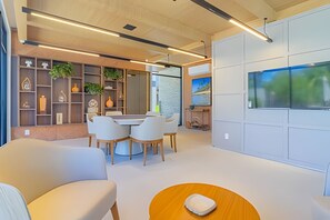 A modern interior with a dining area, white furniture, and a large flat-screen TV mounted on the wall. - Cais Eco Residence beira-mar Muro Alto (Ipojuca)