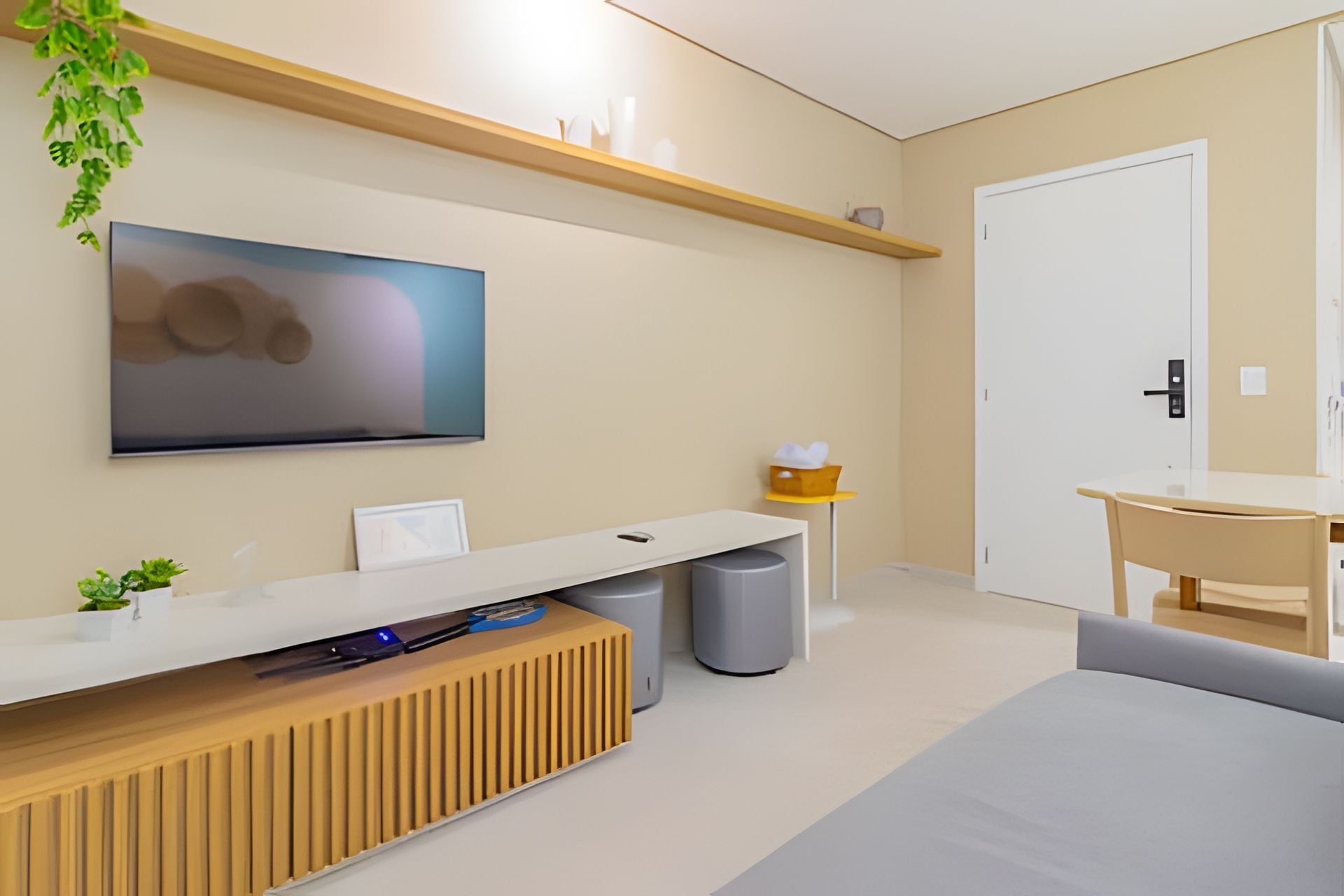 A modern hotel room with a flat-screen TV, a wooden console table, a small plant, a trash bin, and a door with a keycard lock.