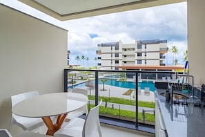 A balcony with a view of a swimming pool and a modern building complex. - Cais Eco Residence beira-mar Muro Alto (Ipojuca)