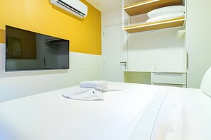 A hotel room with a bed, a window, an air conditioning unit, a mirror, and a built-in shelf with towels. - Cais Eco Residence beira-mar Muro Alto (Ipojuca)