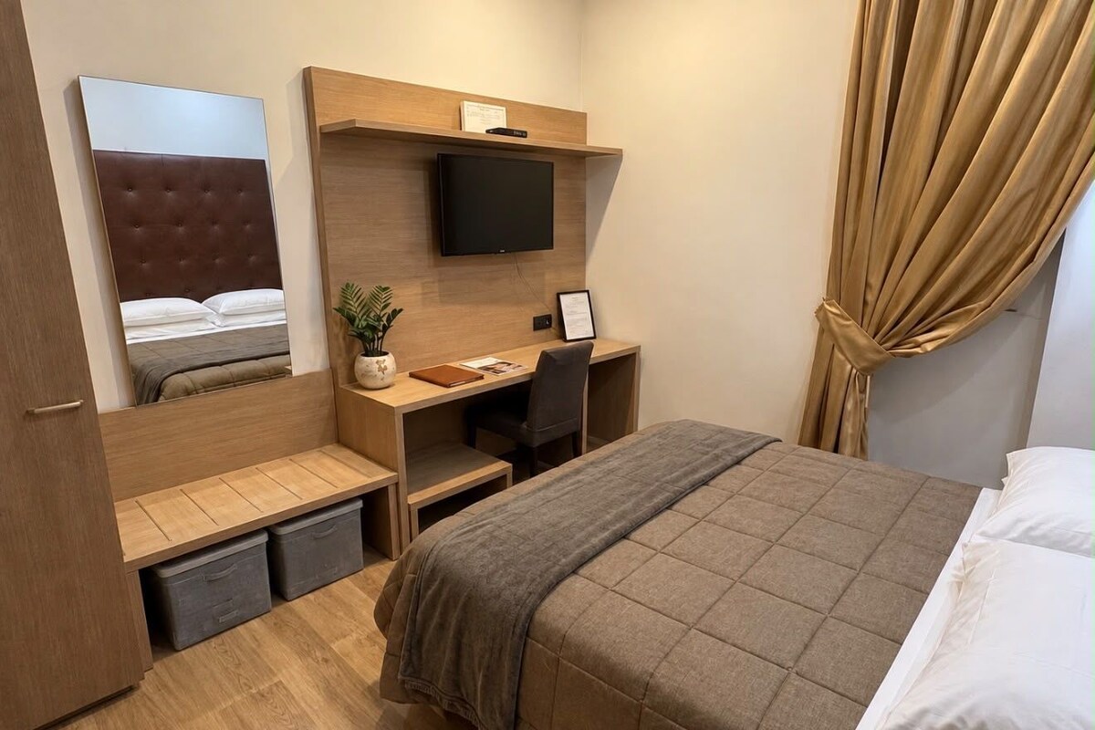 A hotel room with a bed, a desk, a chair, a television, and a wardrobe.