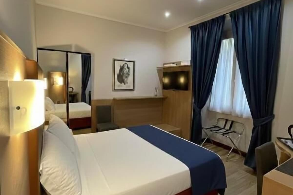 A hotel room with a bed, desk, chair, and a window with curtains.