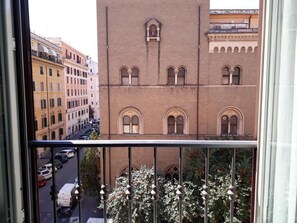 A view from a window overlooking a street with parked cars and a building with arched windows and a statue.