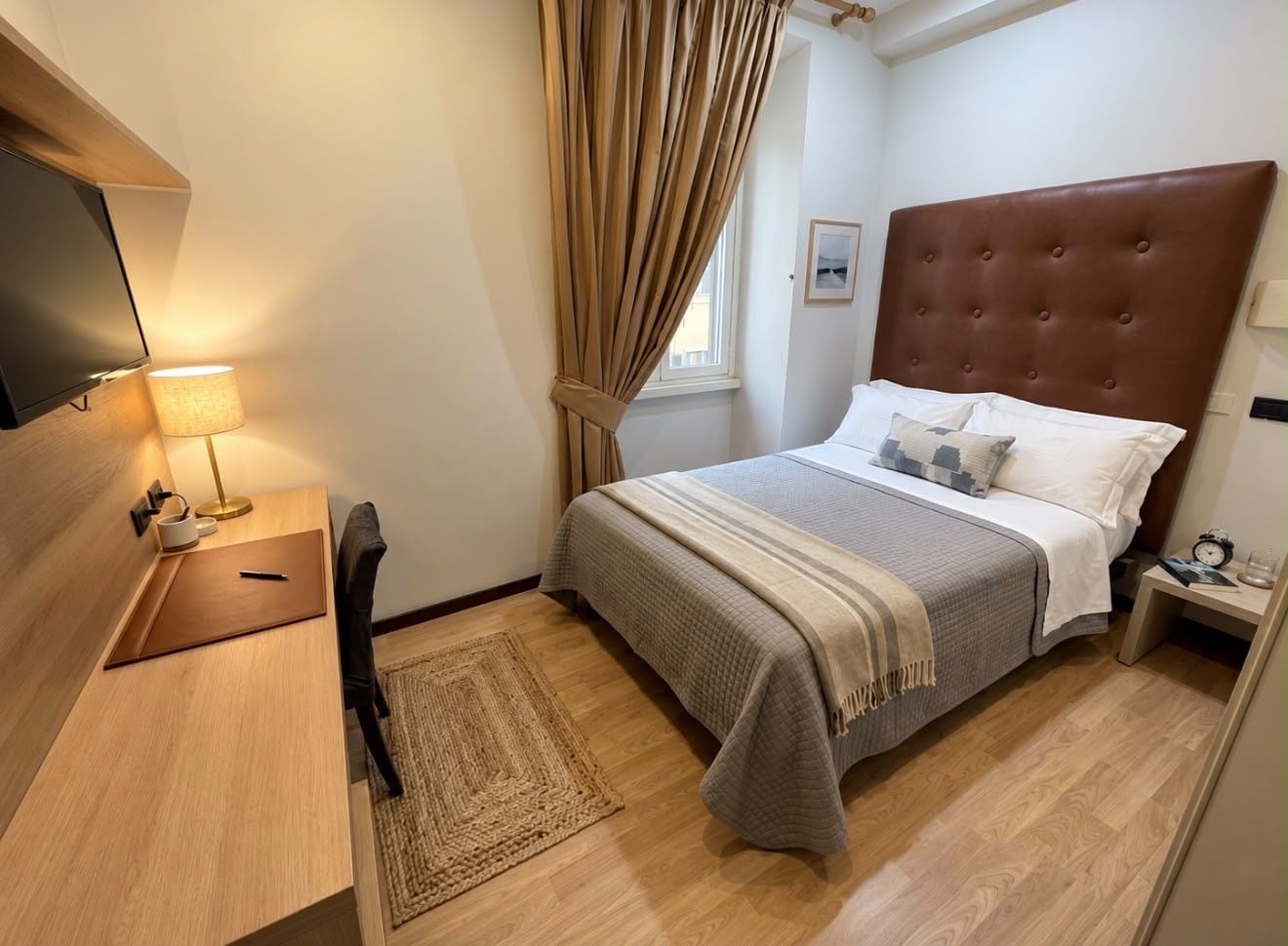 A hotel room with a bed, bedside table, lamp, and a television.