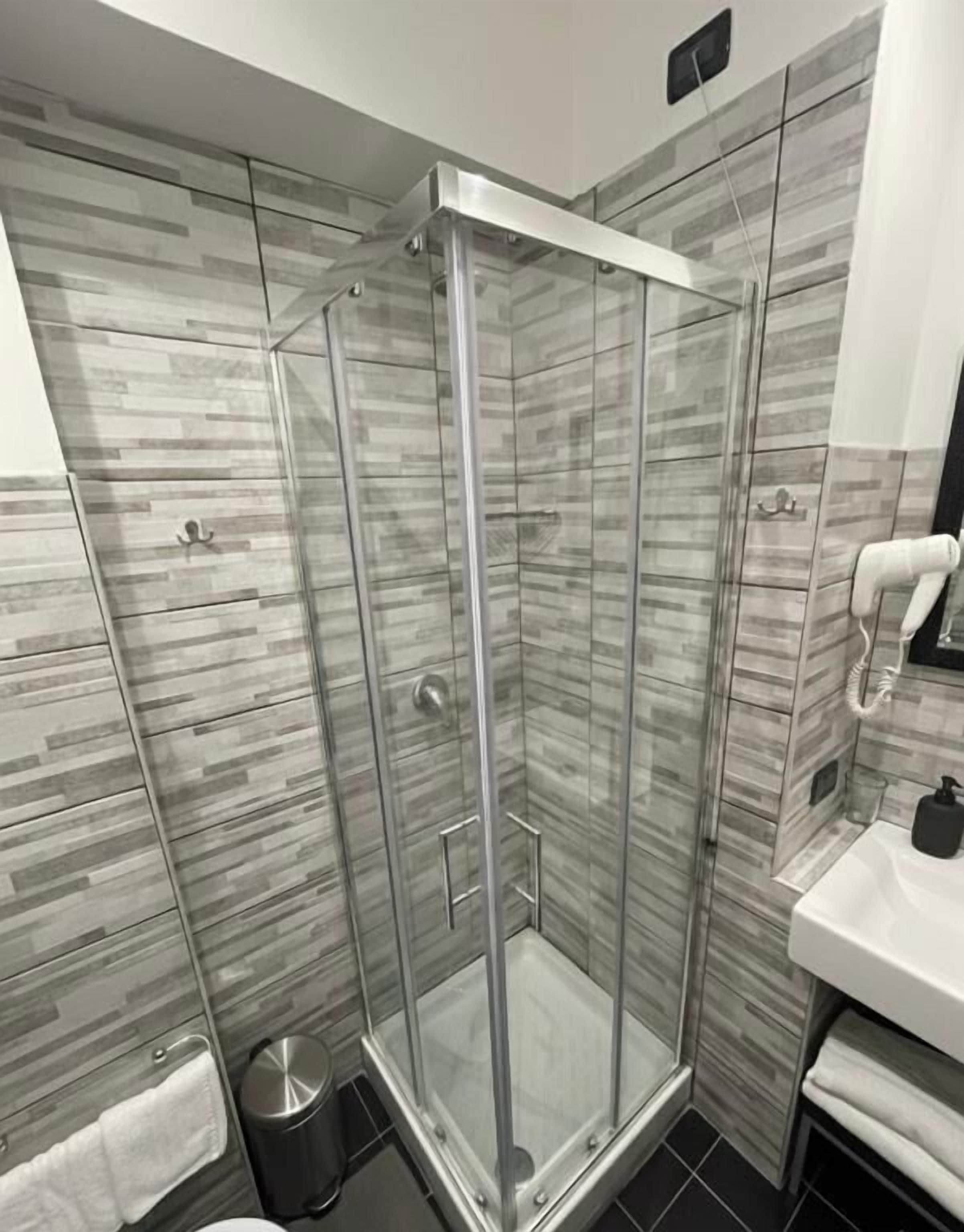 Une salle de bain moderne avec une douche à parois de verre, un lavabo blanc et un mur recouvert de carreaux.