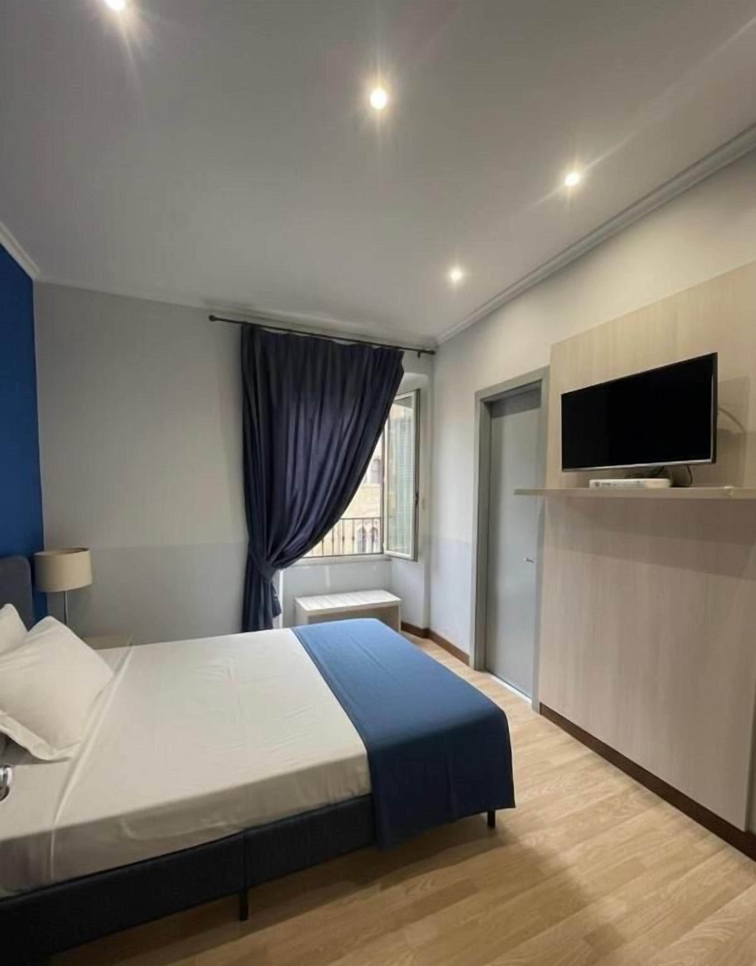 Une chambre d’hôtel avec un lit, un téléviseur fixé au mur et une fenêtre avec des rideaux.