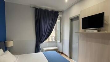 Une chambre d’hôtel avec un lit, un téléviseur fixé au mur et une fenêtre avec des rideaux.