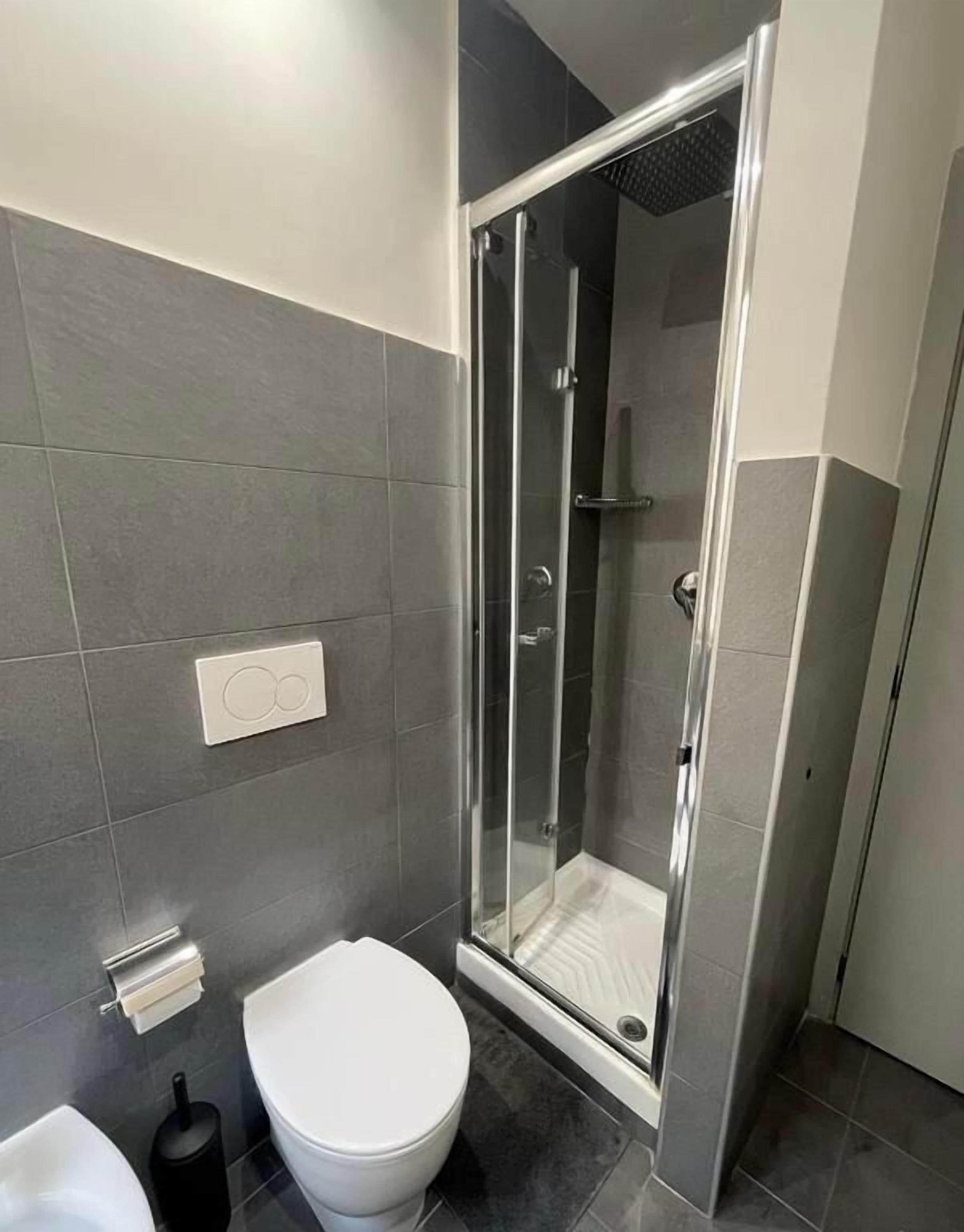 Une salle de bain moderne avec une douche à parois de verre, des toilettes blanches et un sol carrelé foncé.