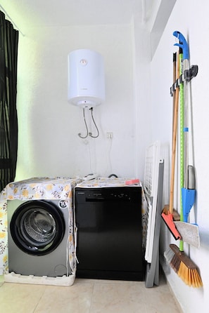 Un espace buanderie compact comprenant un lave-linge et un sèche-linge Bosch, un radiateur et des ustensiles de nettoyage accrochés au mur.