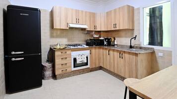 A kitchen with wooden cabinets, a black refrigerator, a stove, and a window with a view.