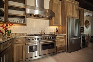 A kitchen with stainless steel appliances, wooden cabinets, and a marble backsplash. - Ocean View Four Bedroom Villa 3 King + bunk – Prana Maya Island Resort (Placencia)
