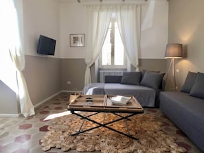 A living room with a sofa, a coffee table, a lamp, and a window with curtains. - Volta 45: An Elegant Loft in the Heart of Testaccio (Roma)