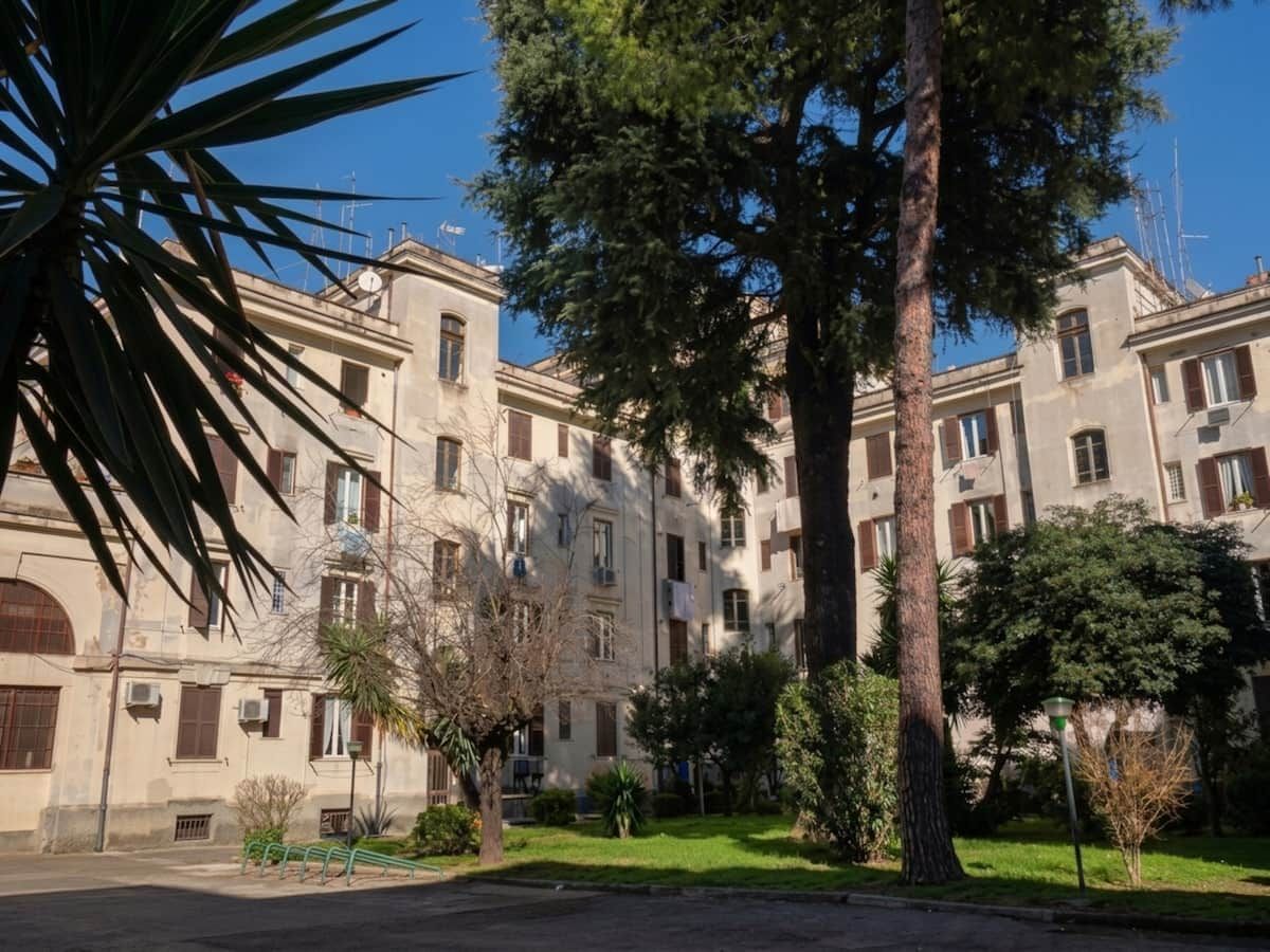 Un immeuble à plusieurs étages doté de balcons, entouré de verdure et d’arbres.