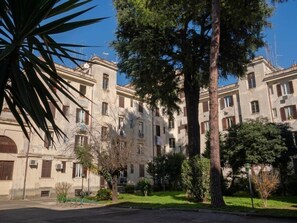 Un immeuble à plusieurs étages doté de balcons, entouré de verdure et d’arbres.