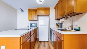 Eine kleine Küche mit Holzschränken, einem weißen Kühlschrank, einem Einbauofen und einem Spülbecken.