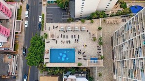 Ein Poolbereich auf dem Dach mit Liegestühlen und einem Schwimmbecken, umgeben von Gebäuden und einer Straße.