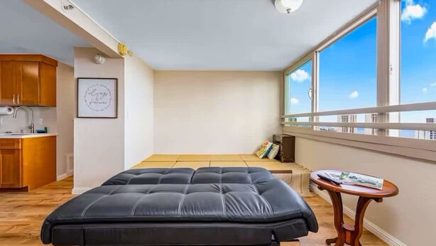 Ein kleines Schlafzimmer mit Bett, Tisch, Fenster mit Aussicht und einer Küchenzeile.