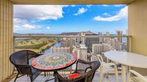 Ein Balkon mit Blick auf einen Fluss und die Skyline, möbliert mit Korbstühlen und einem Tisch.