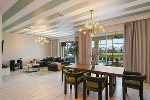 A spacious living room with a dining area, large windows, and a view of the outdoors. - 6BR+Spa&Pool+Walk to Clubhouse+Theater+ThemedRooms (Kissimmee)