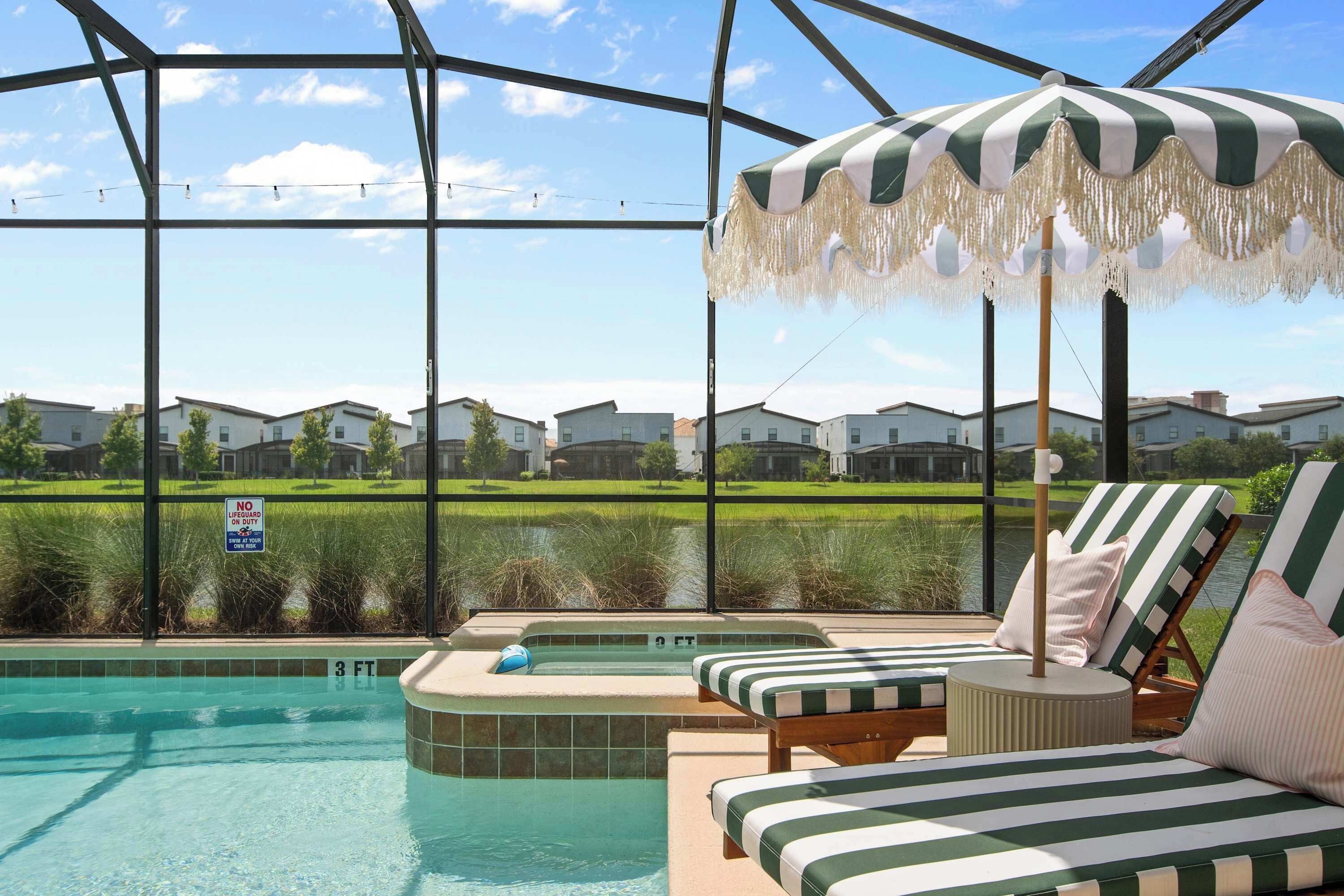 A pool area with a view of houses, a lifeguard sign, and a poolside lounge with striped cushions.
