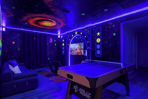 Ein Zimmer mit Tischtennisplatte, einer Couch und einem Fernseher, der ein Videospiel zeigt.