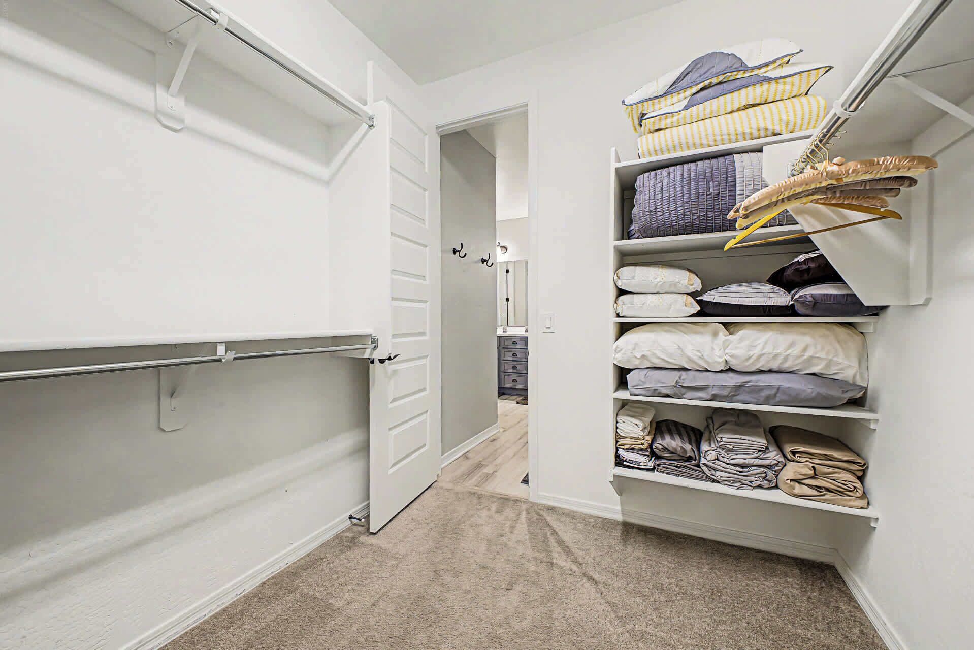 A walk-in closet with open doors, shelves with folded clothes, and a hanging rod.
