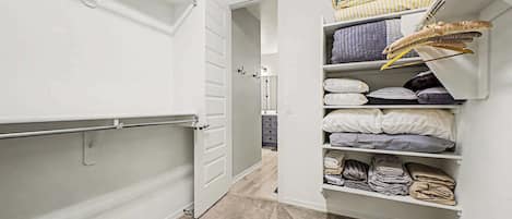 A walk-in closet with open doors, shelves with folded clothes, and a hanging rod.