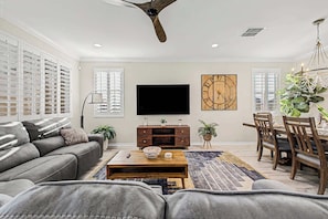 A living room with a sofa, coffee table, TV, and a dining area with chairs and a table. - 4BR Stay | Westgate | Heated Pool, Fire Pit & BBQ (Glendale)