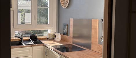 A kitchen with white cabinets, a black stove, a sink, and a window with a view of trees.