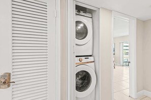 Lavandería con dos lavadoras apiladas, una puerta con cerradura de teclado numérico y vistas a un balcón exterior.