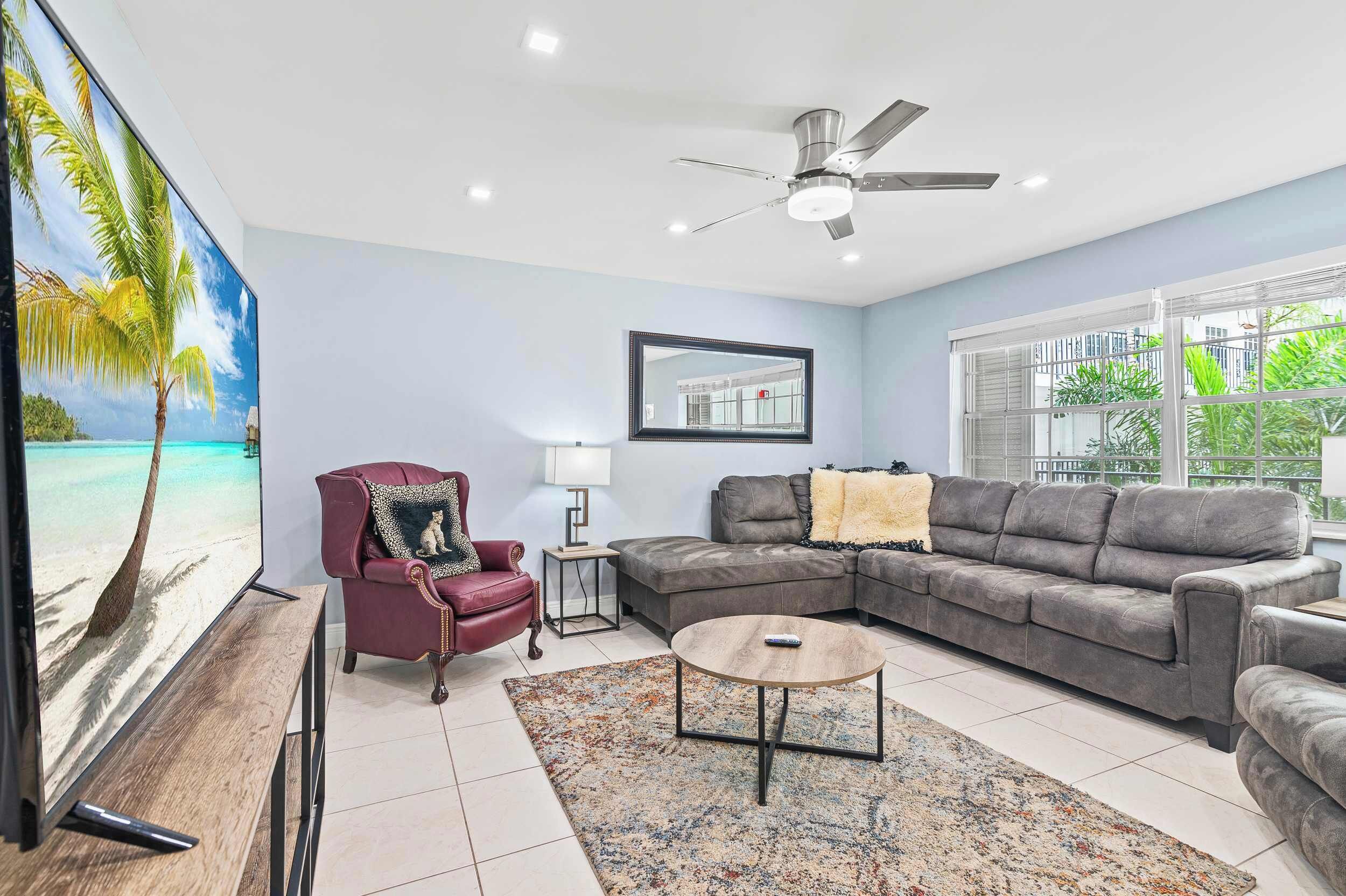 A living room with a red armchair, a grey sofa, a coffee table, and a ceiling fan.