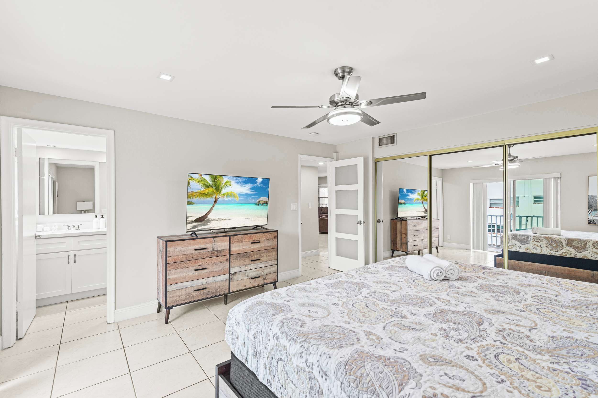 A bedroom with a bed, a television, a wardrobe, and a ceiling fan.