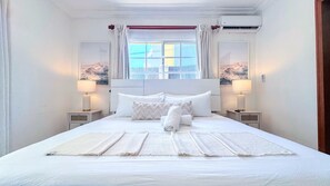Ein Hotelzimmer mit einem großen Bett, zwei Nachttischlampen, einem Fenster mit Vorhängen und einer Klimaanlage.