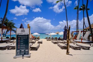 Ein Strand mit Liegestühlen und Sonnenschirmen, ein Schild mit Regeln und freie Sicht auf den Ozean.